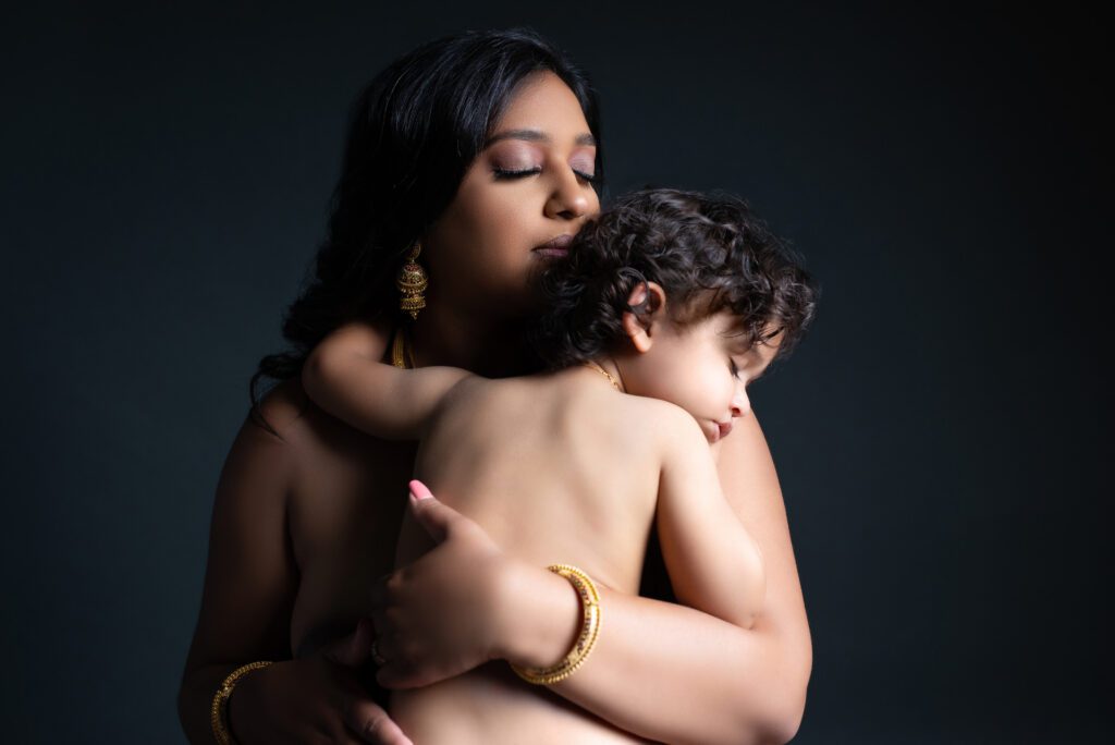 A MOTHER AND HER SON IN AN EMBRACE WHILE HE SLEEPS DURING HER MATERNITY SESSION 